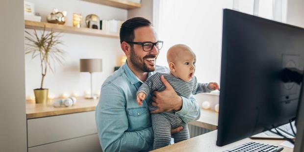 Homem segurando bebê, que olha com cara de surpresa para tela de computador.